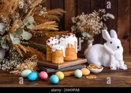 Osterkuchen und Eier in verschiedenen Farben mit Osterhase auf Holzhintergrund gemalt Stockfoto