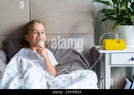 Kleines Mädchen im Bett mit Vernebler oder Inhalator, Kind macht Inhalation zu Hause Stockfoto