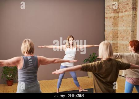 Junger selbstbewusster Fitnesstrainer mit ausgestreckten Armen, der reifen Weibchen neue Übungen zeigt, während er vor ihnen steht Stockfoto