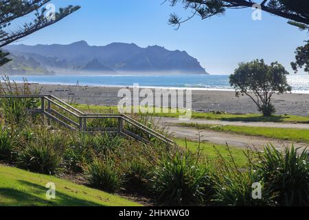 Ein sonniger Strand an der Tokomaru Bay in der Region Gisborne, Neuseeland. Holztreppen führen hinunter in den Sand Stockfoto