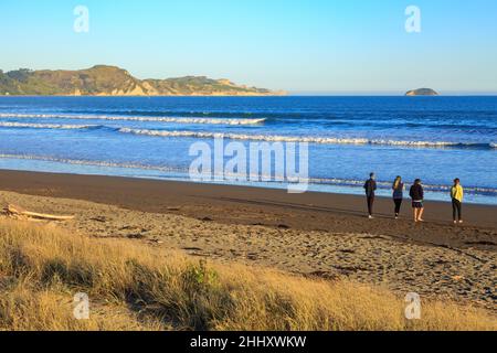 Eine Gruppe von Menschen am Waikanae Beach, Gisborne, Neuseeland, blickt bei warmem Licht am späten Nachmittag auf das Wasser der Poverty Bay Stockfoto