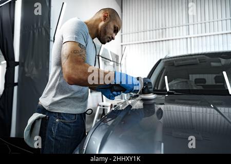 Fahrzeugdetails. Männliche Hände mit Orbitalpolierer in der Autowerkstatt Stockfoto