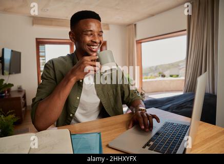 Junger Erwachsener schwarzer Mann hält Morgenkaffee arbeiten entfernt in modernen Wohnung. Stockfoto