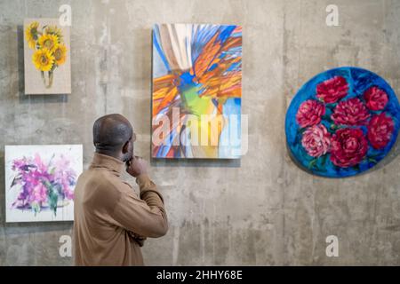 Afrikanischer junger Mann, der die moderne Kunst an der Wand untersucht, während er die Kunstgalerie besucht Stockfoto
