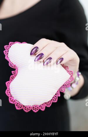Weibliche Hände mit lila langen Nägeln halten ein weiß rosa Herz Stockfoto