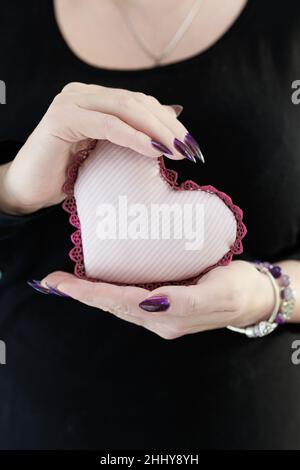 Weibliche Hände mit lila langen Nägeln halten ein weiß rosa Herz Stockfoto