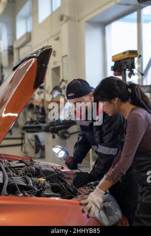 Zwei junge interkulturelle Mechaniker in der Arbeitskleidung biegen über Dieselmotor des Autos, während es vor der Reparatur zu überprüfen Stockfoto