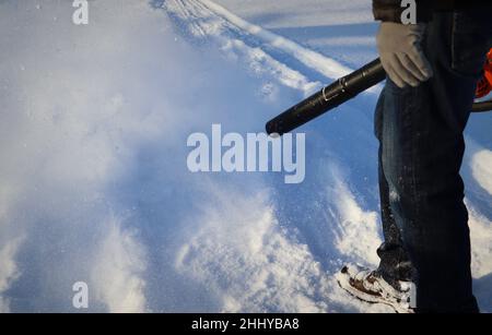 Mann reinigt Bürgersteig von Schnee mit Gebläse Stockfoto