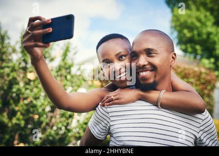 Teile dein Glück mit der Welt. Ausgeschnittene Aufnahme eines glücklichen jungen Paares, das draußen ein Selfie macht. Stockfoto