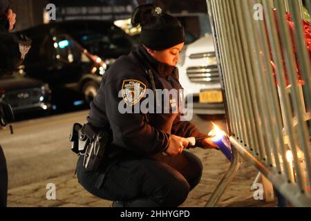 New York, Usa. 24th Januar 2022. Ein Polizeibeamter zündet vor dem Polizeiprävier von 32nd in Harlem eine Kerze an, während sie den Polizisten Jason Rivera und Wilbert Mora Tribut zollt. Polizeibeamte und die Öffentlichkeit zündeten Kerzen an, legten Blumen und respektierten die gefallenen Beamten. Kredit: SOPA Images Limited/Alamy Live Nachrichten Stockfoto