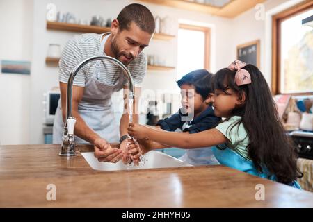 Waschen wir diese Keime weg. Ein kurzer Schuss eines Mannes und seiner beiden Kinder, die sich im Küchenbecken die Hände waschen. Stockfoto