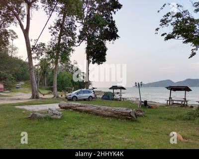 Camping und Zelt und SUV-Auto unter der Kiefer in der Nähe des Strandes mit Sonnenuntergang Himmel und kleine Insel am Horizont. Endau, Malaysia Stockfoto