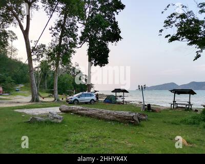 Camping und Zelt und SUV-Auto unter der Kiefer in der Nähe des Strandes mit Sonnenuntergang Himmel und kleine Insel am Horizont. Endau, Malaysia Stockfoto