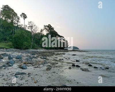 Seascape mit Felsbrocken und Meereswellen schlagen sich an einem Sommertag gegen Fels. Wunderschöner tropischer Strand mit Sonnenuntergangshimmel und Blick auf die kleine Insel am Horizont. Stockfoto