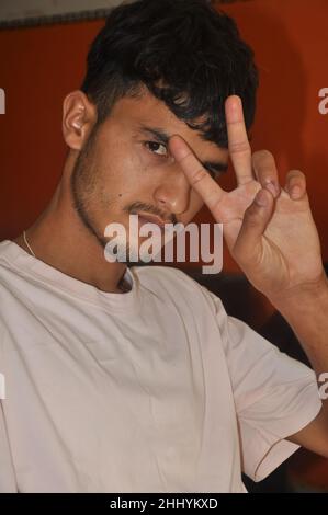 Nahaufnahme eines hübschen jungen Mannes, der mit seiner Hand ein Friedenszeichen zeigt und drinnen mit Blick auf die Kamera sitzt Stockfoto