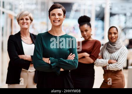 Vertrauen bringt wirklich Erfolg. Porträt einer jungen Geschäftsfrau, die in einem Büro mit ihren Kollegen im Hintergrund steht. Stockfoto
