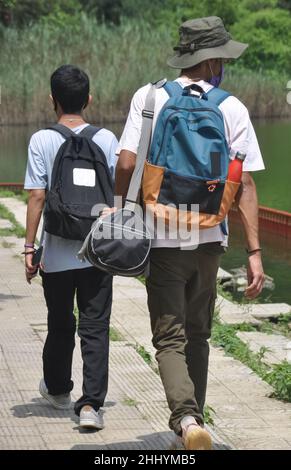 Rückansicht von zwei männlichen Touristen, die Gesichtsmaske mit Rucksack tragen und am See spazieren gehen. Reisen während einer Coronavirus-Pandemie Stockfoto