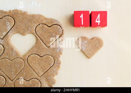 Der Teig wird in Form eines Herzens und Holzwürfeln mit der Zahl 14 geschnitten. Das Konzept des Feiertagsbackens zum Valentinstag. Draufsicht. Stockfoto