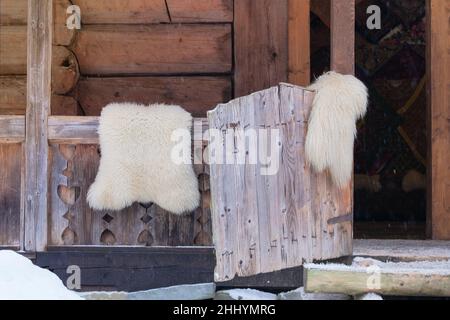 Gegerbte Schaffellteppiche hängen an einem Zaun in einem Holzhaus auf dem Land. Reise-, Tourismus- und Umweltkonzept. Stockfoto