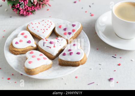 Lebkuchen mit weißer Glasur bedeckt und auf einer hellen Untertasse mit einer Tasse Espresso und Blumen im Hintergrund bestreuen. Das Konzept des Feierns Stockfoto