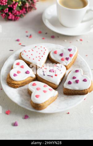 Lebkuchen mit weißer Glasur bedeckt und auf einer hellen Untertasse mit einer Tasse Espresso und Blumen im Hintergrund bestreuen. Das Konzept des Feierns Stockfoto