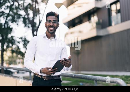Porträt eines lächelnden jungen schwarzen Geschäftsmannes, der ein Tablet mit den Händen hält Stockfoto