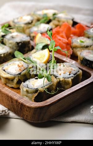 Nahaufnahme heiße Sushi-Brötchen. Gebackene Brötchen mit Garnelen auf einem Holzgerät. Bambusstäbchen und Sojasauce. Stockfoto