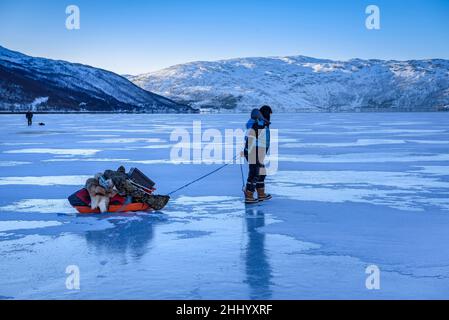 Ein Fischer, der an einem frostigen kalten Wintertag auf dem gefrorenen Nordfjord in der Nähe von Tromsø angeln geht (Tromsø, Norwegen) ESP: Pescador yendo ein Pescar Stockfoto