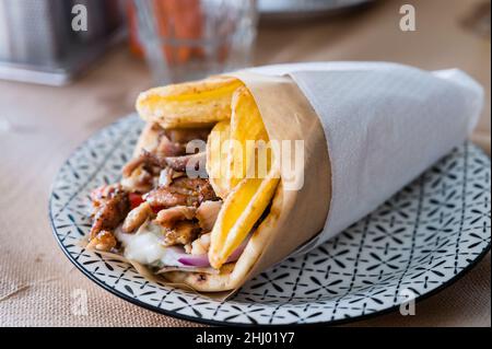 Traditionelle griechische Küche Gyros Pita mit Pommes frites, Gemüse und Tzatziki-Sauce. Nahaufnahme eines Kebab-Sandwiches auf Kreta, Griechenland. Traditionelle griechische Küche. Stockfoto