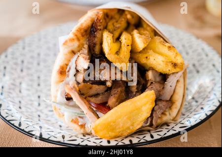 Traditionelle griechische Küche Gyros Pita mit Pommes frites, Gemüse und Tzatziki-Sauce. Nahaufnahme eines Kebab-Sandwiches auf Kreta, Griechenland. Traditionelle griechische Küche. Stockfoto