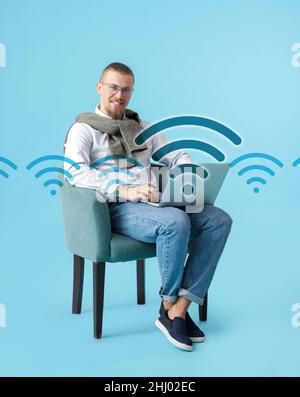 Junger Mann mit Laptop, der Wi-Fi auf farbigem Hintergrund verwendet Stockfoto