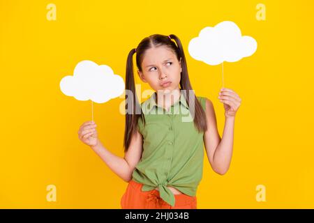 Foto von ziemlich zweifelhaft preteen Mädchen gekleidet grün oben halten zwei sprechende Wolken suchen leeren Raum isoliert gelben Hintergrund Stockfoto