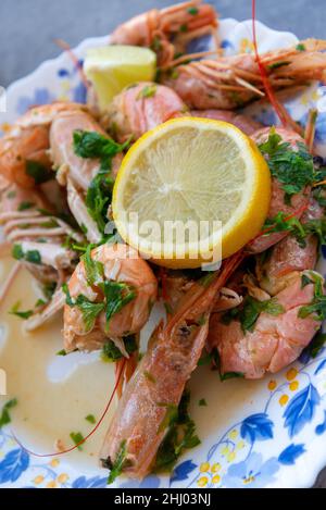 Frische Garnelen und Langustinen auf einem Teller serviert mit grüner Petersilie und einer Scheibe Zitrone. Mediterrane Küche Stockfoto