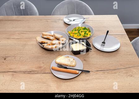 Frühstück mit Rührei, Wurst und Sandwiches auf einem Holztisch im Speisesaal. Stockfoto