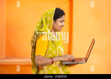 Junge indische Frau trägt Sari mit Laptop. Frau trägt traditionelle Tücher halten Lerncomputer vor orangefarbenem Hintergrund. Geschicklichkeit indien conce Stockfoto