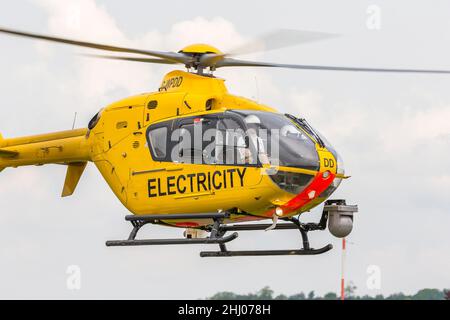 Gelber WPD-Hubschrauber (wird in der Stromverteilungsbranche für die Wartung/Reparatur von Netzwerken/Inspektion von Stromleitungen verwendet), der isoliert am Himmel fliegt. Stockfoto