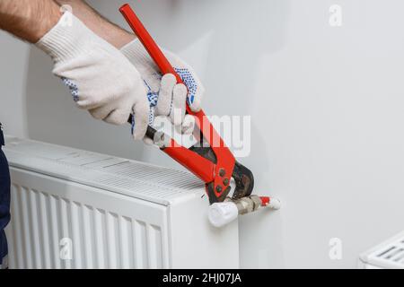 Ein Arbeiter in einem orangefarbenen Helm installiert Heizkörper im Haus Stockfoto