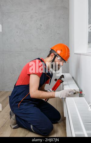 Ein Arbeiter in einem orangefarbenen Helm installiert Heizkörper im Haus Stockfoto