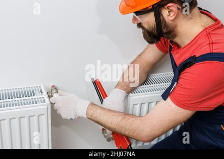 Ein Arbeiter in einem orangefarbenen Helm installiert Heizkörper im Haus Stockfoto