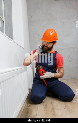 Ein Arbeiter in einem orangefarbenen Helm installiert Heizkörper im Haus Stockfoto