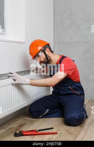 Ein Arbeiter in einem orangefarbenen Helm installiert Heizkörper im Haus Stockfoto