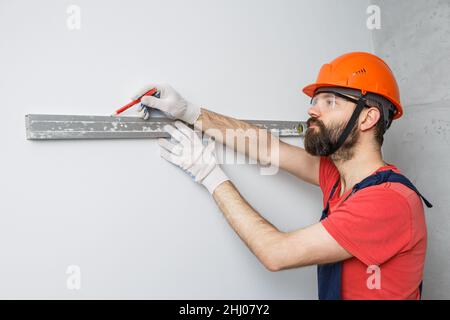 Ein Arbeiter in einem orangefarbenen Helm überprüft die Wände mit einem Wasserstand Stockfoto