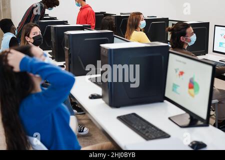 Multirassische junge Studenten, die während des Coronavirus-Ausbruchs im Technikraum Computer benutzen – Fokus auf das richtige Mädchengesicht Stockfoto