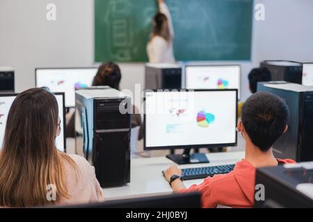 Multirassische Schüler, die in der Business-Klasse Computer mit Sicherheitsmasken in der Schule benutzen - Fokus auf den rechten Kopf des Jungen Stockfoto