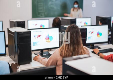 Multirassische Studenten, die während der Business Class Computer benutzen, tragen Sicherheitsmasken in der Schule - konzentrieren Sie sich auf den Kopf eines Mädchens in der Mitte Stockfoto