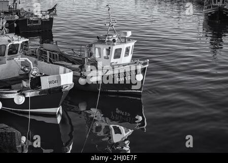 Zwei kleine Fischerboote werden zusammen vertäut und spiegeln sich im Wasser. Andere Boote sind im Hintergrund. Stockfoto