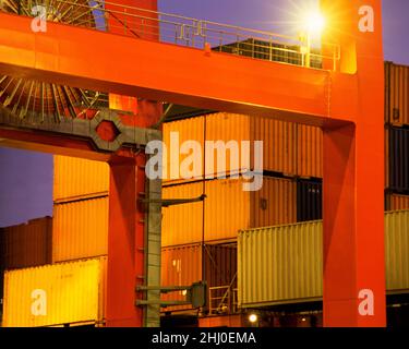 Frachtcontainer im Industriehafen gestapelt. Nahaufnahme des Portalkrans bei Nacht. Containerstapelung am Hafen. Die Infrastruktur ist beleuchtet. Stockfoto