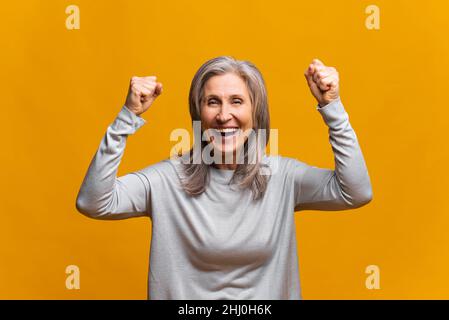 Porträt einer aufgeregt überglücklich modisch gekleideten Frau, die mit erhobenen Fäusten steht und schreit yeah, ich bin Sieger, freue mich über den Sieg, Erfolg.Studio auf gelbem Hintergrund gedreht Stockfoto