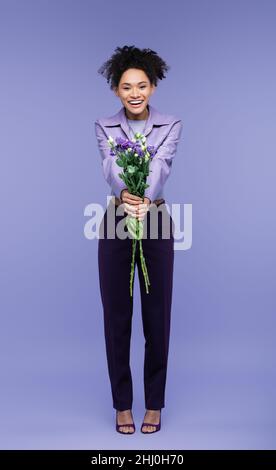 Volle Länge der positiven afroamerikanischen Frau mit Blumenstrauß auf lila Stockfoto