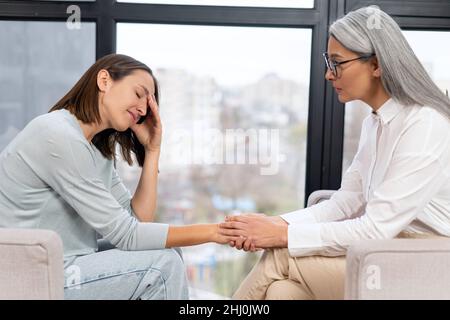 Leitender grauhaariger Therapeut drückt einer verärgerten Patientin während der Therapiesitzung Unterstützung und Empathie aus. Konzept der psychischen Gesundheit Stockfoto